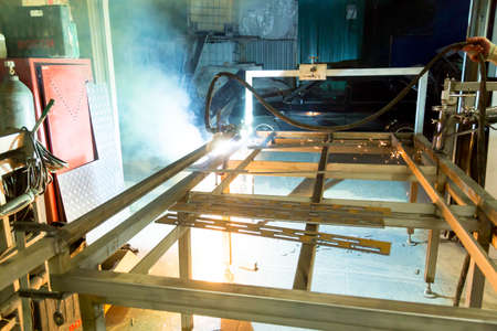 Plasma cutting machine burns through a thick sheet of steel by scattering drops of molten metal in...