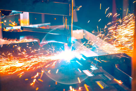 Plasma cutting machine burns through a thick sheet of steel by scattering drops of molten metal in different directionsの写真素材