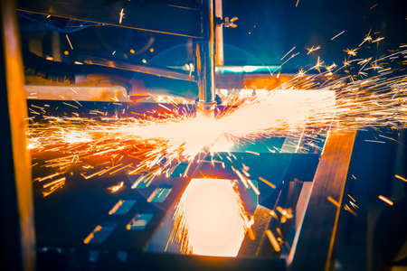 Plasma cutting machine burns through a thick sheet of steel by scattering drops of molten metal in...