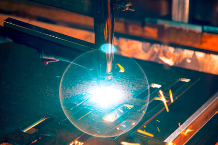 Plasma cutting machine burns through a thick sheet of steel by scattering drops of molten metal in...