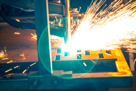Plasma cutting machine burns through a thick sheet of steel by scattering drops of molten metal in...