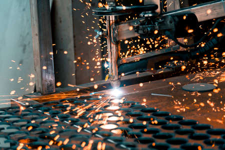Plasma cutting machine burns through a thick sheet of steel by scattering drops of molten metal in...