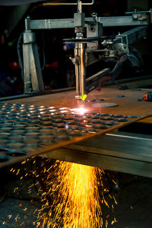 Plasma cutting machine burns through a thick sheet of steel by scattering drops of molten metal in different directionsの写真素材
