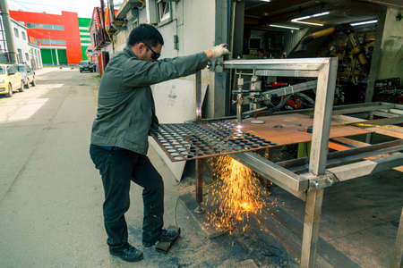 A worker cuts thick sheet steel with a plasma machine, scattering drops of molten steel in dif-ferent directionsの写真素材