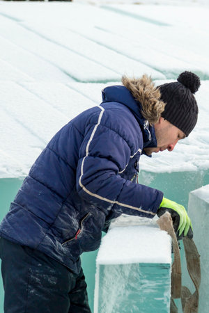 Worker assembler in jacket and black hat unloads ice blocksの写真素材