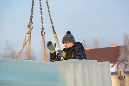 Portrait of a worker slinger in a blue jacket unloading ice blocks using a chain spider