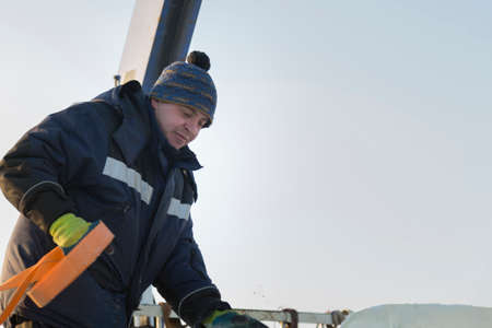 Portrait of a worker slinger in a blue jacket unloading ice blocks using a chain spider