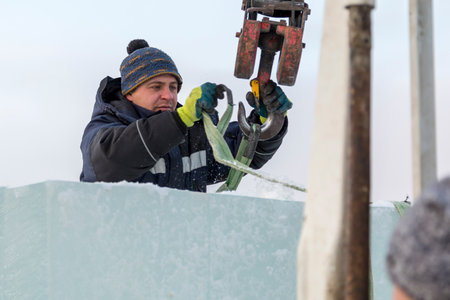 Portrait of a worker slinger in a blue jacket unloading ice blocks using a chain spider