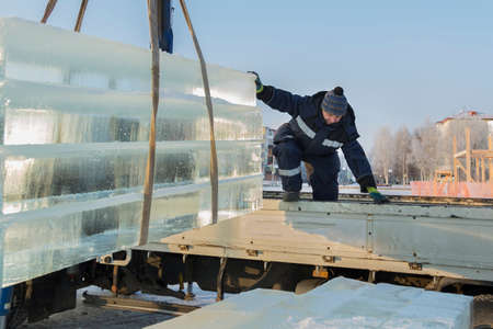 Portrait of a worker slinger in a blue jacket unloading ice blocks using a chain spiderの写真素材