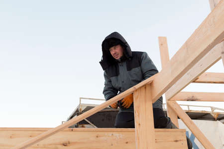 An installer in a blue jacket mounts the frame of a slide made of wooden beamsの写真素材