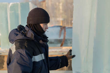 Portrait of a working assembler in a blue jacket and a knitted black hat near an ice panelの写真素材