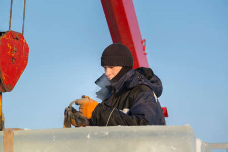 Worker assembler in jacket and black hat unloads ice blocks