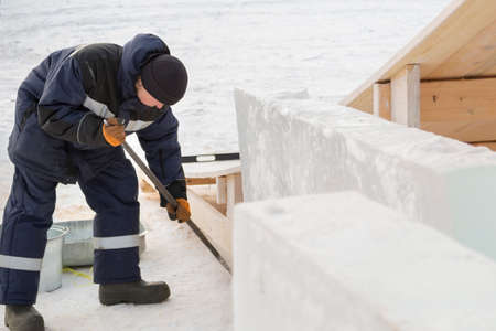 Worker assembler in jacket and black hat unloads ice blocksの写真素材