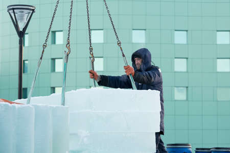 Slinger assembler in a blue jacket with a hood and a black hat unloads ice blocksの写真素材