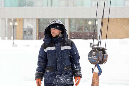A worker assembler in winter overalls with a shovel and an iron trough walks along the con-struction siteの写真素材