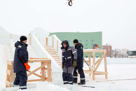 Three workers cover the frame of a wooden slide with ice panels