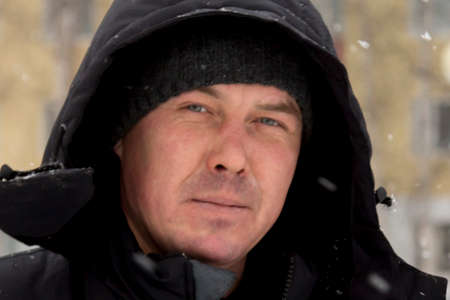 Builder in a gray hooded jacket with a hammer in his hand at the assembly of a wooden struc-ture