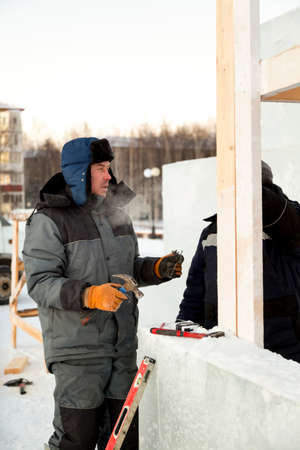 Builder in a gray hooded jacket with a hammer in his hand at the assembly of a wooden struc-tureの写真素材