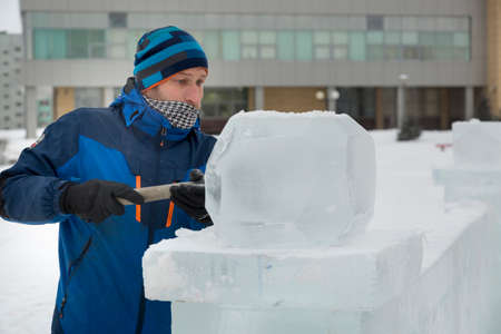 The sculptor cuts an ice figure out of ice with a chisel for Christmasの写真素材