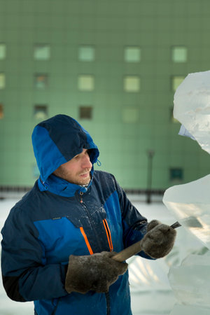 The sculptor cuts an ice figure from a block of ice with a chisel for CHRISTMAS being on a wooden...