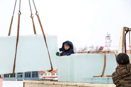 Workers in winter suits wind slings under an ice block at a construction siteの写真素材