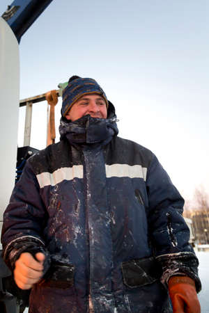 Portrait of a worker in a blue jacket with a hood at the hook of a truck crane