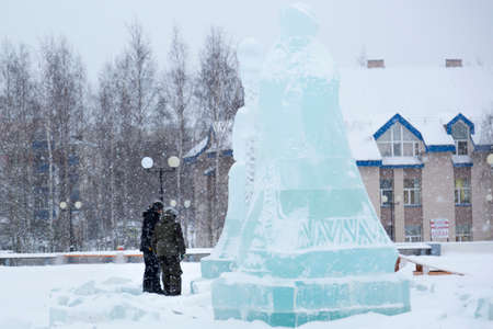 Two workers at a construction site are carving an elegant Christmas composition into an ice panel with a petrol saw.の写真素材