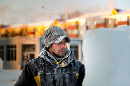 Portrait of a working assembler in a winter jacket and a black cap with a visor near the ice fig-ure