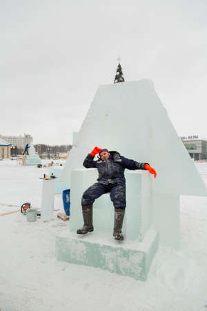 Portrait of a working assembler in a winter jacket and a knitted black hat on an ice throne