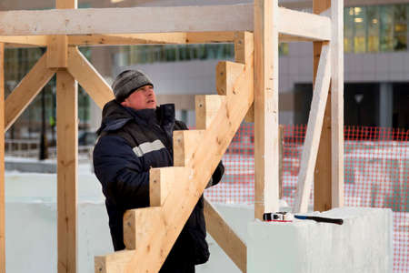 Portrait of a fitter in a blue jacket and a knitted hat at the frame of a wooden slide