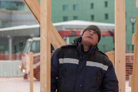 A builder in a blue jacket with a hammer in his hand hammers a nail