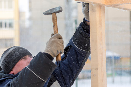 Worker in a jacket with a hood and a woolen knitted hat at the workplace