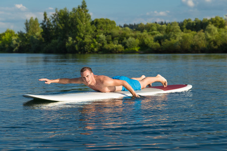 Young attractive man swiming on stand up paddle board in the lake, SUPの写真素材