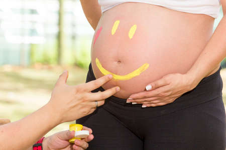 Pregnant woman belly, baby father hand drawing happy face.