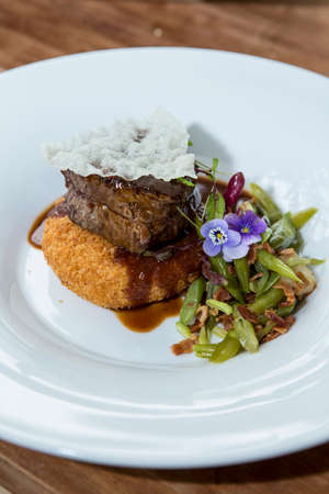 Tasty portion of meat cooked in its sauce on a bed of gratin mashed potatoes, accompanied by...