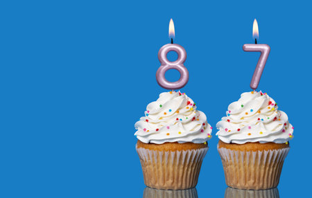 Birthday Cupcakes With Candles Lit Forming The Number 87 - Photo On Blue Background