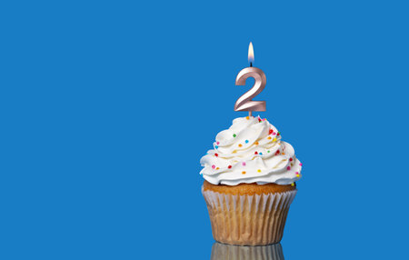 Birthday Or Anniversary Cupcake with Lit Candle; Number 2 Candle - Photo On Blue Background.の写真素材