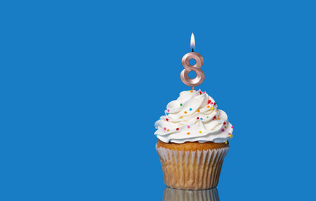 Birthday Or Anniversary Cupcake with Lit Candle; Number 8 Candle - Photo On Blue Background.の写真素材