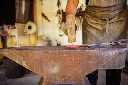 A blacksmith is hitting a piece of hot metal with the hammer on the anvilの写真素材