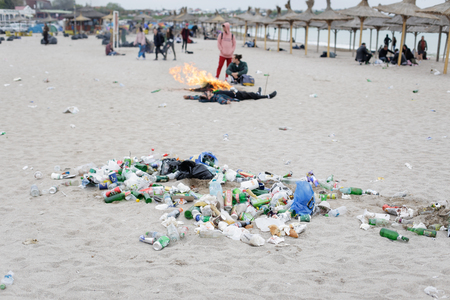 VAMA VECHE, ROMANIA - MAY 1, 2018: Young people rest on the beach amongst debris (especially empty bottles), after partying all night, early in the morning just before sunriseのeditorial素材