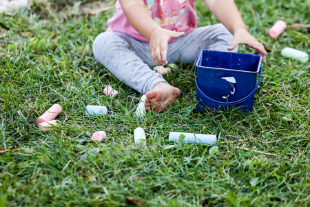 Details of a young girl playing with colored chalk on the grass, in the front yard of a kindergarten...