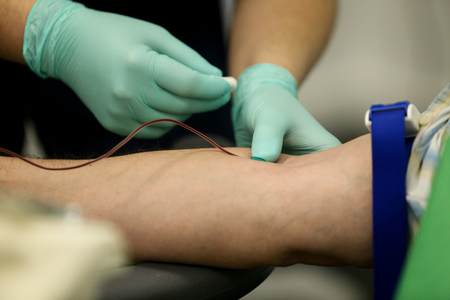 Details with the hands of a doctor, wearing rubber surgical gloves, taking blood from the vein of a patient with a catheterの写真素材