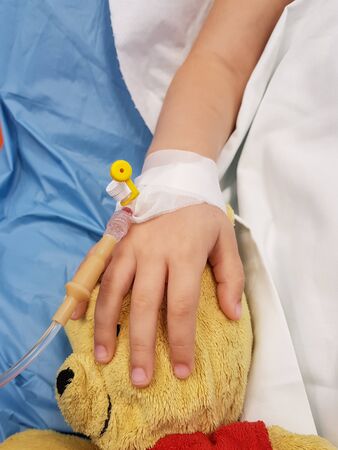 Details with the hand of an ill little girl in a pediatric hospital reserve, with a cannula and holding a teddy bearの写真素材