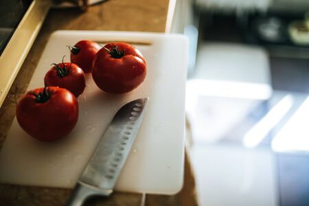 Freshly picked tomatoes from the garden in the kitchen on a plastic cutting board and near a chef knifeの写真素材
