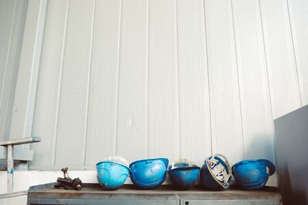 Dirty blue worker helmets on top of an old, rusty and dirty workbench in a workshop