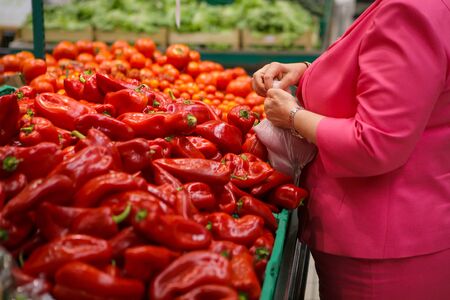 Woman choosing red sweet peppers on the fruits and vegetables aisle in a store.の写真素材