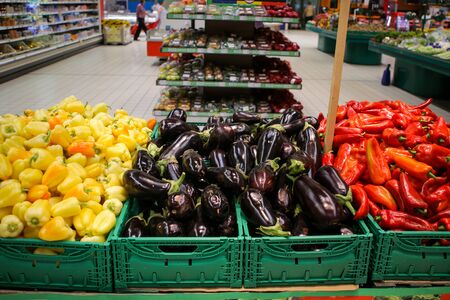 Red sweet peppers, eggplants and yellow sweet peppers on the fruits and vegetables aisle in a storeの写真素材