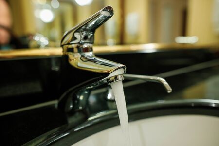 Shallow depth of field (selective focus) image with water running from a faucet and a soap dispenser in a hotel bathroom.の写真素材