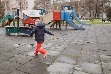 Little girl playing and jumping in rain puddle on an empty kids playground during a winter day in Bucharest, Romania.の写真素材
