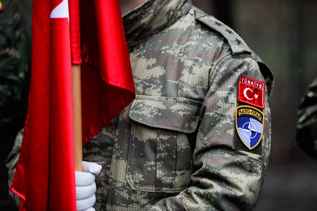 Shallow depth of field image (selective focus) with details of a Turkish army soldier holding a flag and having Turkey and NATO insignia. Turkey and NATO relationship.のeditorial素材